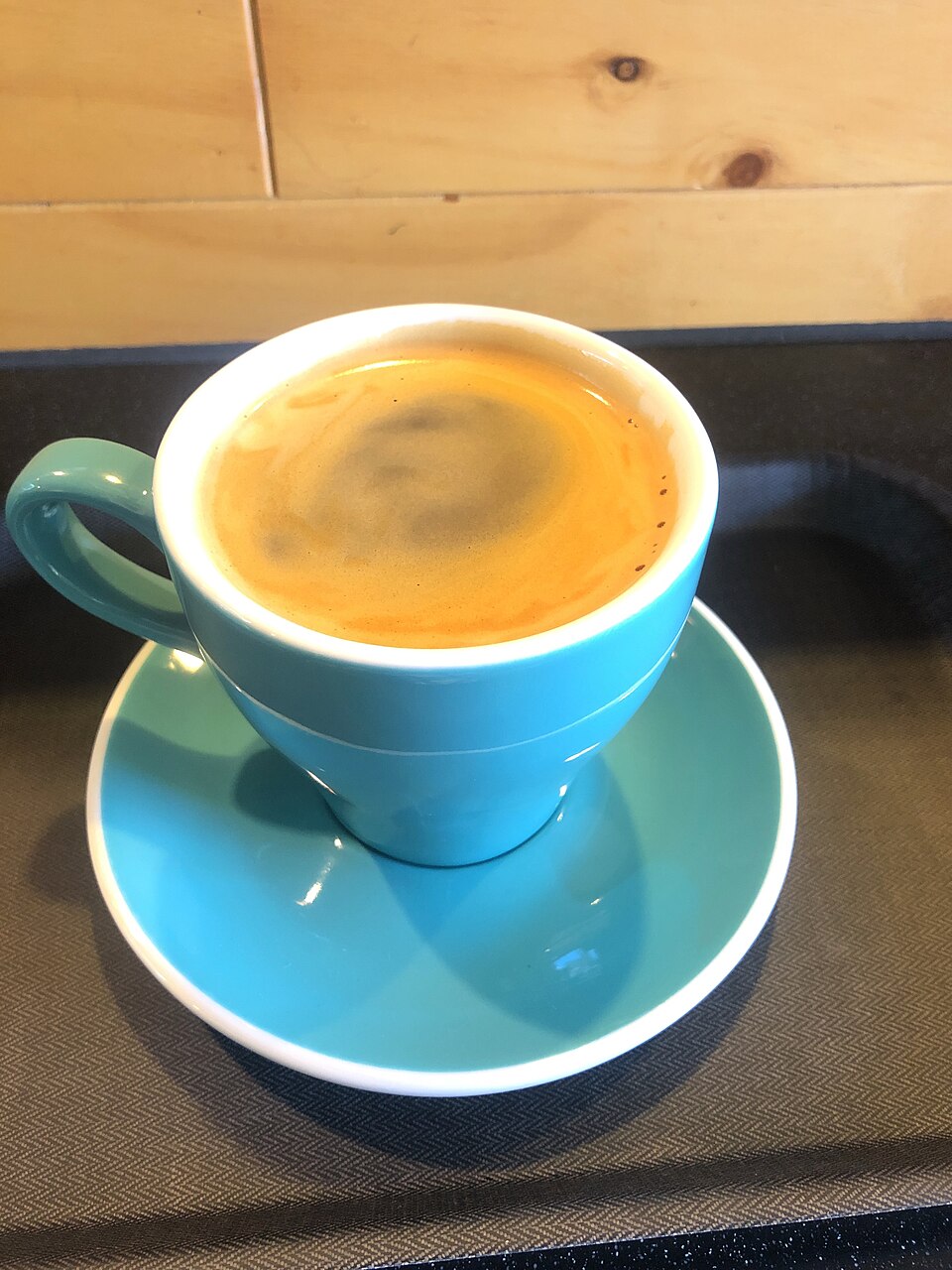 Café negro en taza de cerámica turquesa sobre platito, con crema en la superficie