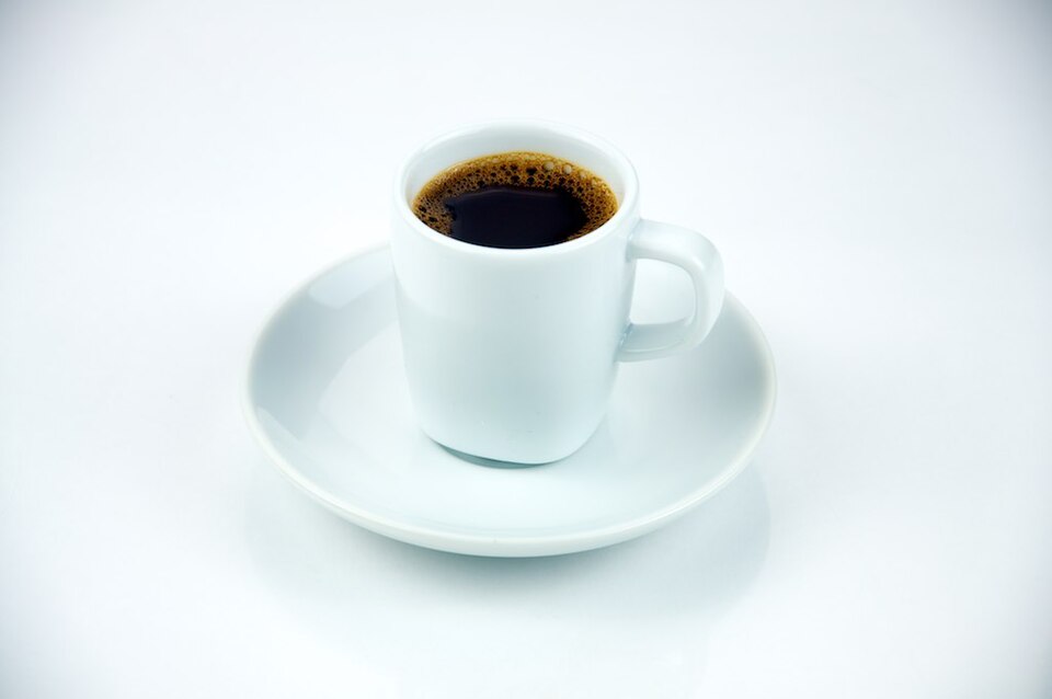 Taza de espresso blanca sobre plato, fondo neutro y luz cenital